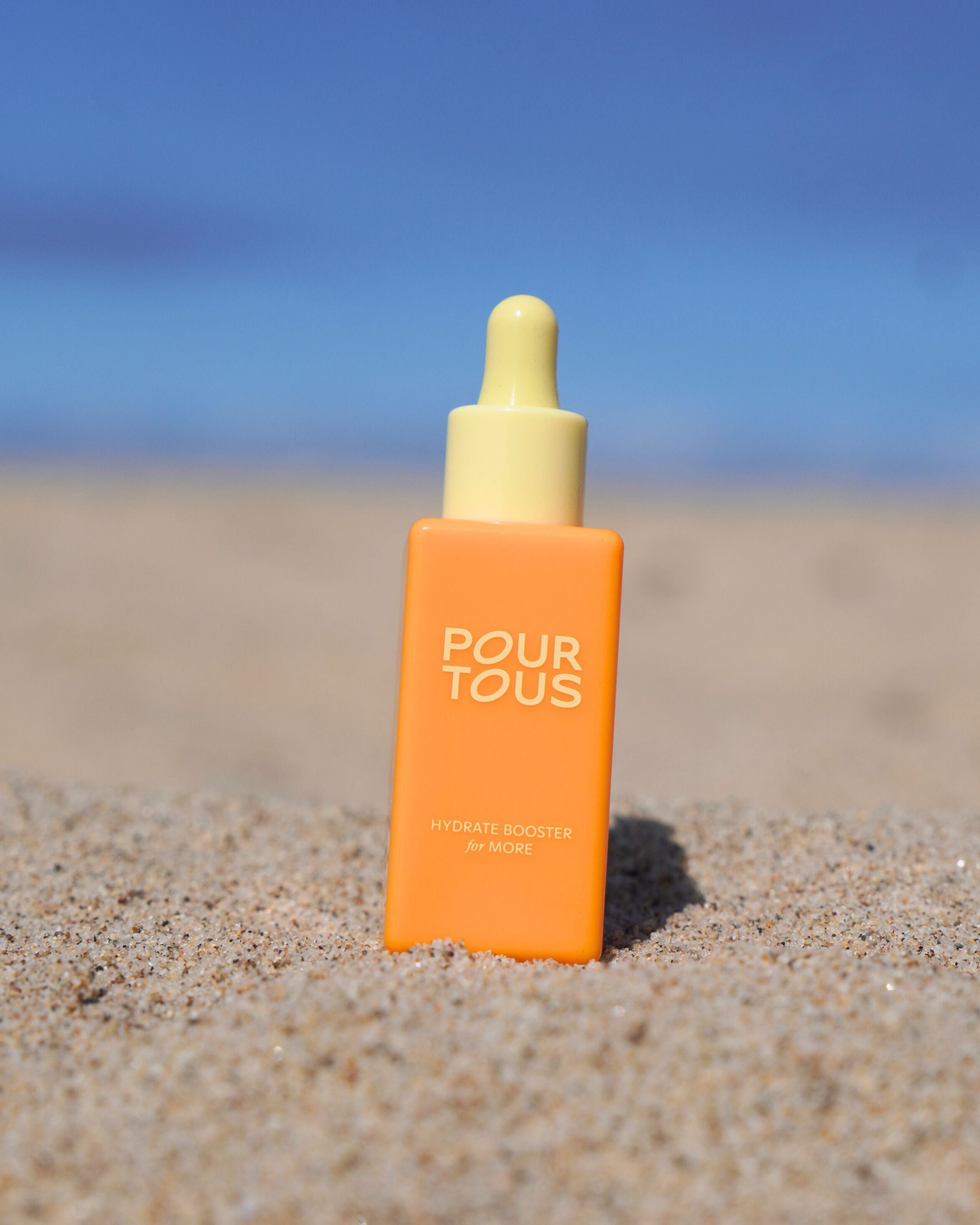 Orange serum bottle on sandy beach with blue sky