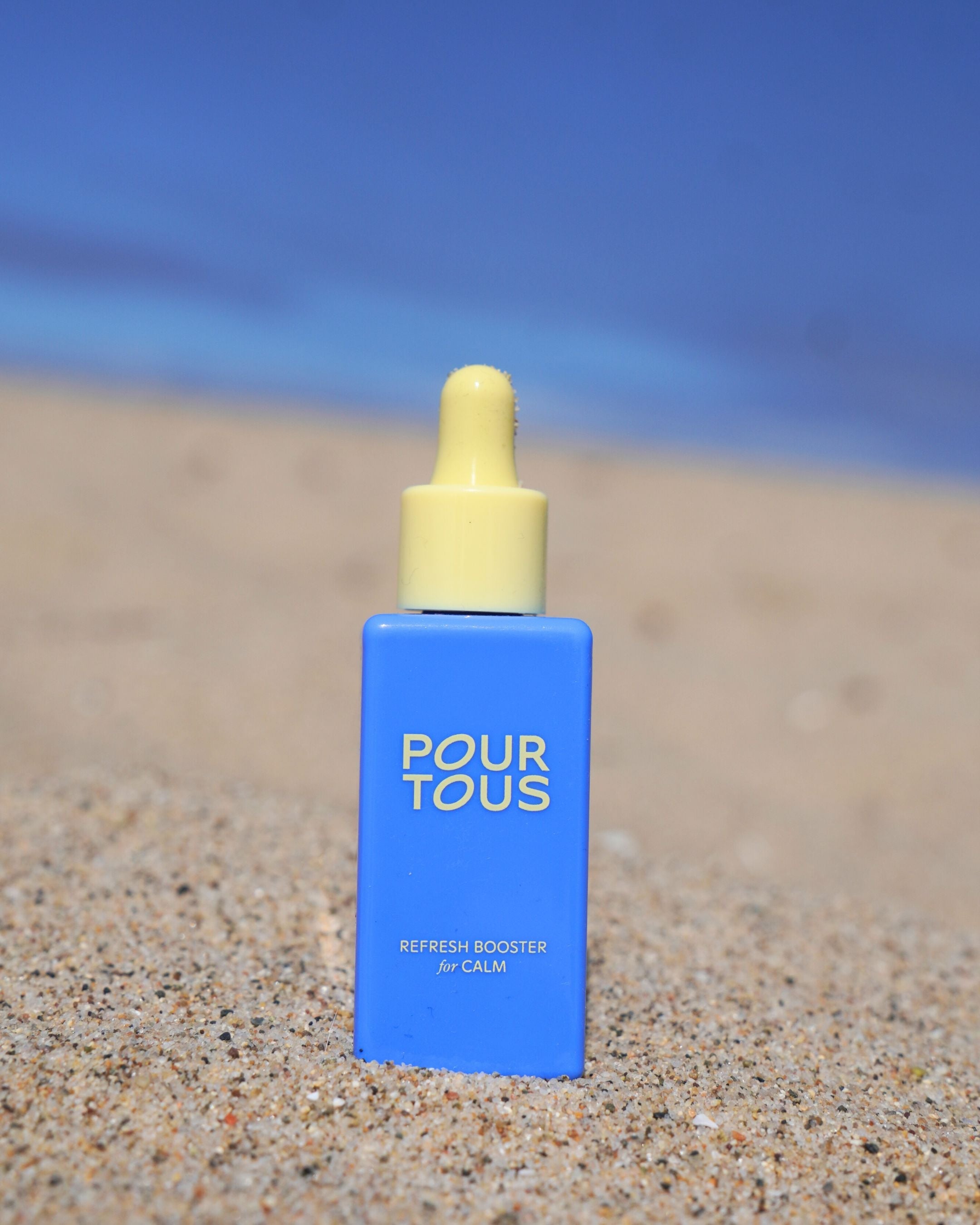 Blue dropper bottle on sandy beach with blue sky background.