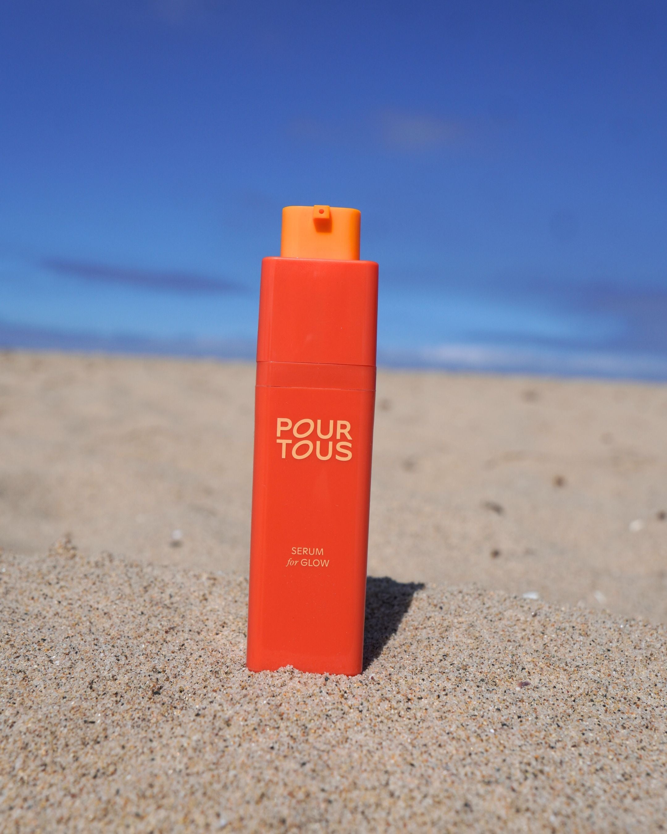Orange serum bottle on sandy beach under blue sky.